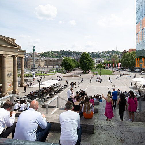 Blick von der Treppe am kleinen Schlossplatz auf die Königstraße und den Schlossplatz. Auf der Treppe sitzen Menschen.