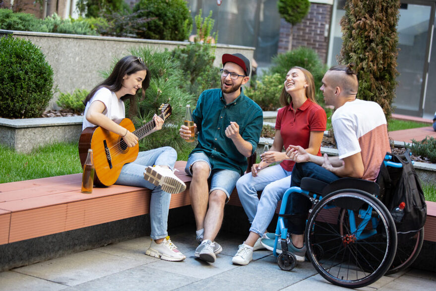 Gruppe von Freunden, die an einem Sommertag auf Bank sitzen und Musik machen