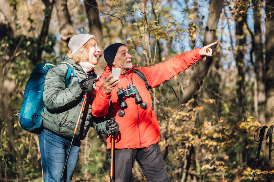 Ein Mann zeigt seiner Frau etwas in der Natur. Bei haben Rucksäcke bei sich und Ferngläser.