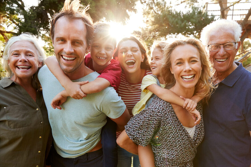 Gruppenbild einer Mehrgenerationenfamilie, die fröhlich in die Kamera lacht