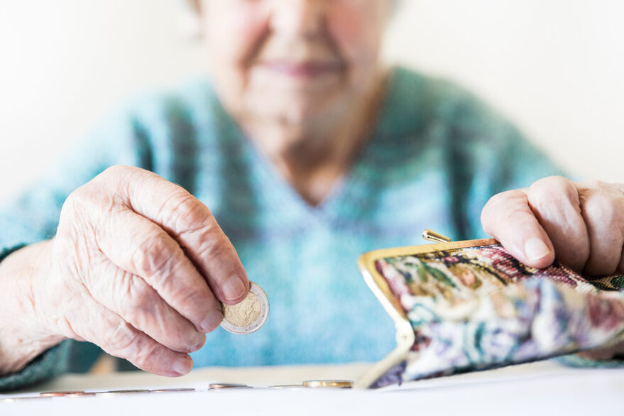 Eine alte Frau holt aus ihrer Brieftasche Geldmünzen und legt diese auf den Tisch.