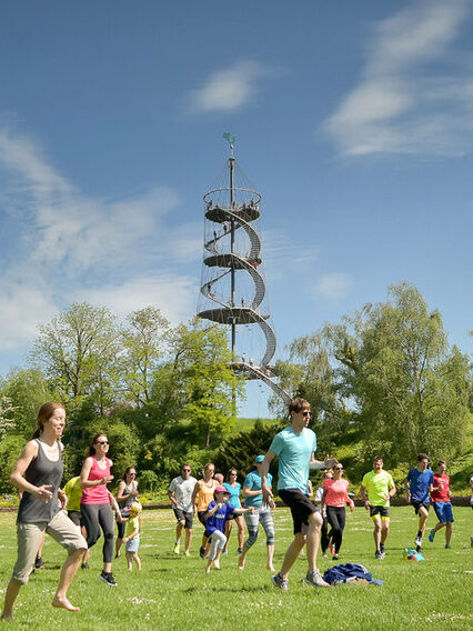 Mehrere Menschen machen Sport im Park, im Hintergrund ist ein Aussichtsturm zu sehen.