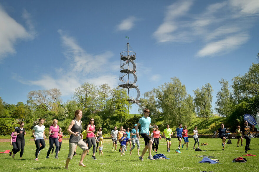 Mehrere Menschen machen Sport im Park, im Hintergrund ist ein Aussichtsturm zu sehen.