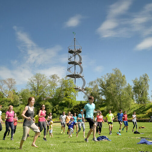 Mehrere Menschen machen Sport im Park, im Hintergrund ist ein Aussichtsturm zu sehen.