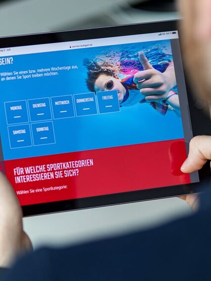 Ein Mann hält ein Tablet in den Händen. Auf dem Display ist eine Online-Anwendung zu sehen mit einem tauchenden Schwimmer.