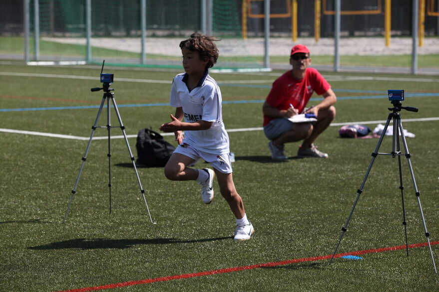 Ein Junge sprintet über ein Sportplatz, ein Trainer beobaxhtet ihn.