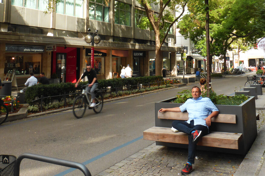 Blick in die Eberhardstraße. Eine Person sitzt auf einer Bank an einem Pflanzenkübel.