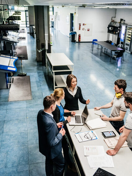 Eine Gruppe von Ingeniueren diskutiert in einer Fabrikhalle diverse Energieeffizienzmaßnahmen.