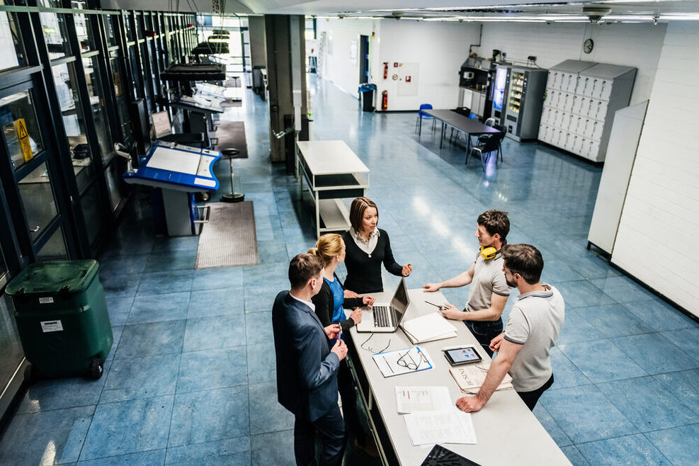 Eine Gruppe von Ingeniueren diskutiert in einer Fabrikhalle diverse Energieeffizienzmaßnahmen.