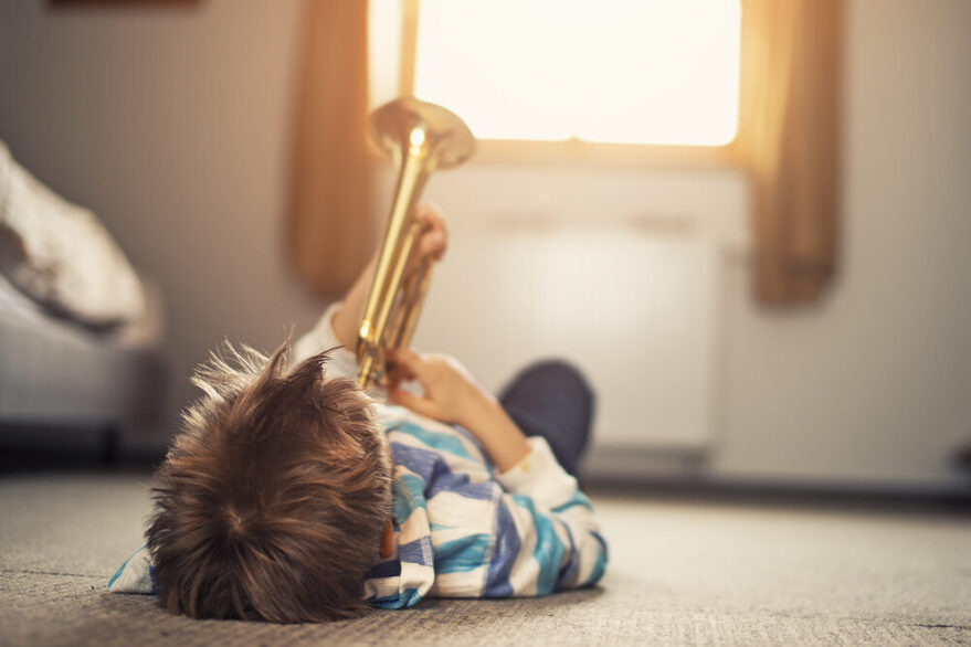 Kleiner Junge spielt auf dem Rücken liegend Trompete