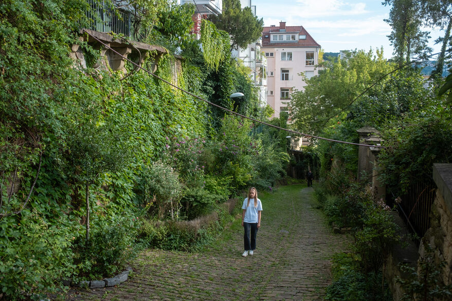 Eine junge Frau läuft langsam einen dicht mit Grünpflanzen bewucherten Weg in Stuttgart hinauf.