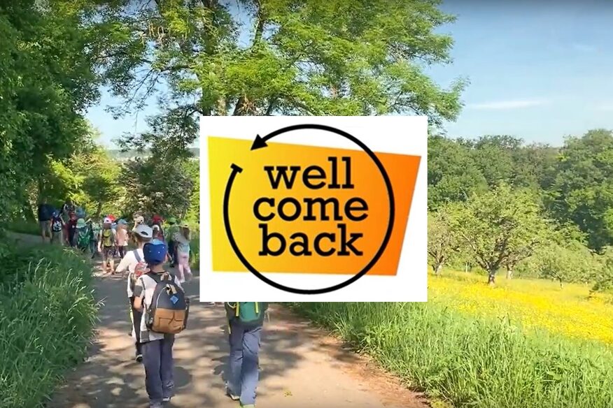 Eine Schulklasse läuft auf einem Weg durch die Natur. In der Mitte vom Bild ist ein Logo mit dem Projekttitel "wellcomeback“.