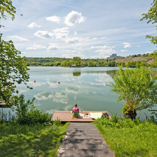 Eine Frau sitzt am Ufer eines Sees auf einem Steg.
