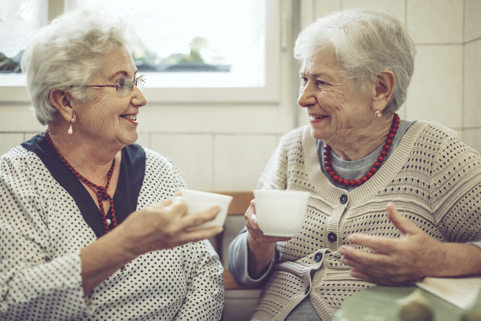 Zwei ältere Frauen trinken zusammen Kaffee in einer Küche.