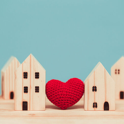 Ein hölzernes Modell zeigt sechs Häusschen mit einem gestricktne, roten Herz in der Mitte.