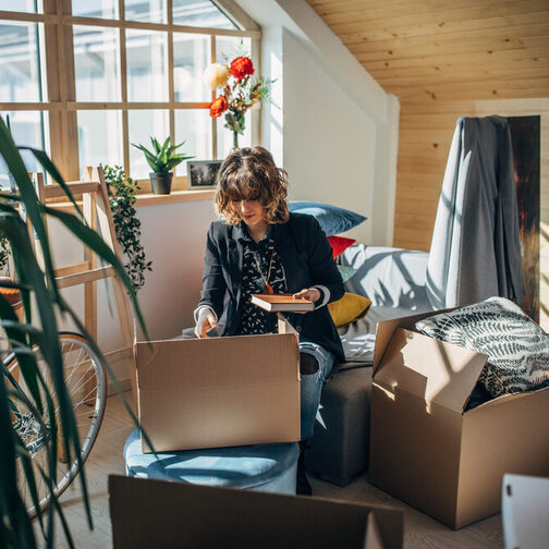 Eine junge Frau räumt Umzugskartons in einer Wohnung aus.