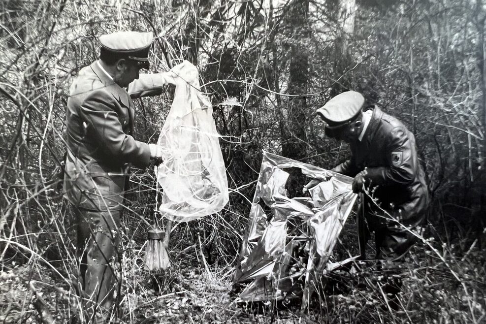 Zwei Männer vom Vollzugsdienst finden einem Gebüsch zwei große Plastiktüten.