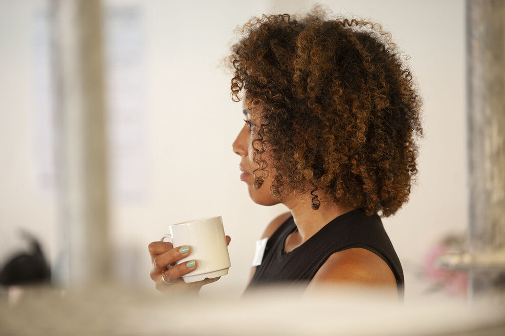 Eine Teilnehmerin mit Tasse in der Hand hört zu.