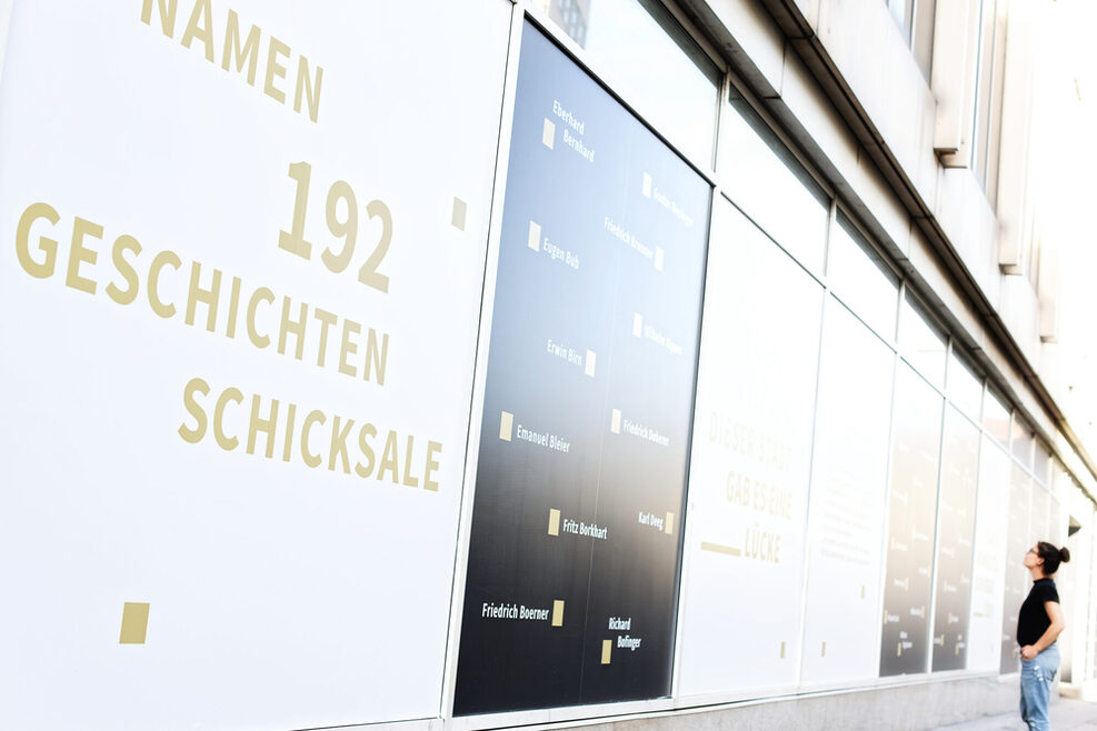 Eine Frau steht vor einer mit schwarzen und weißen Folien beklebten Wand, die Informationen zur Ausstellung „Die doppelte Lücke“ im Stuttgarter Rathaus zeigt.