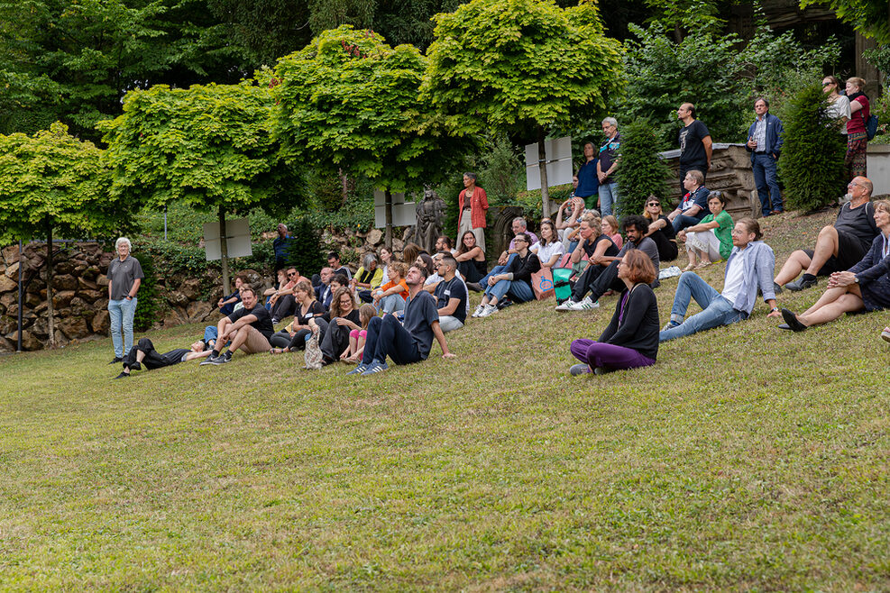 Mehrere Menschen sitzen entspannt auf der grünen Wiese am Hang des Städtischen Lapidariums in Stuttgart.