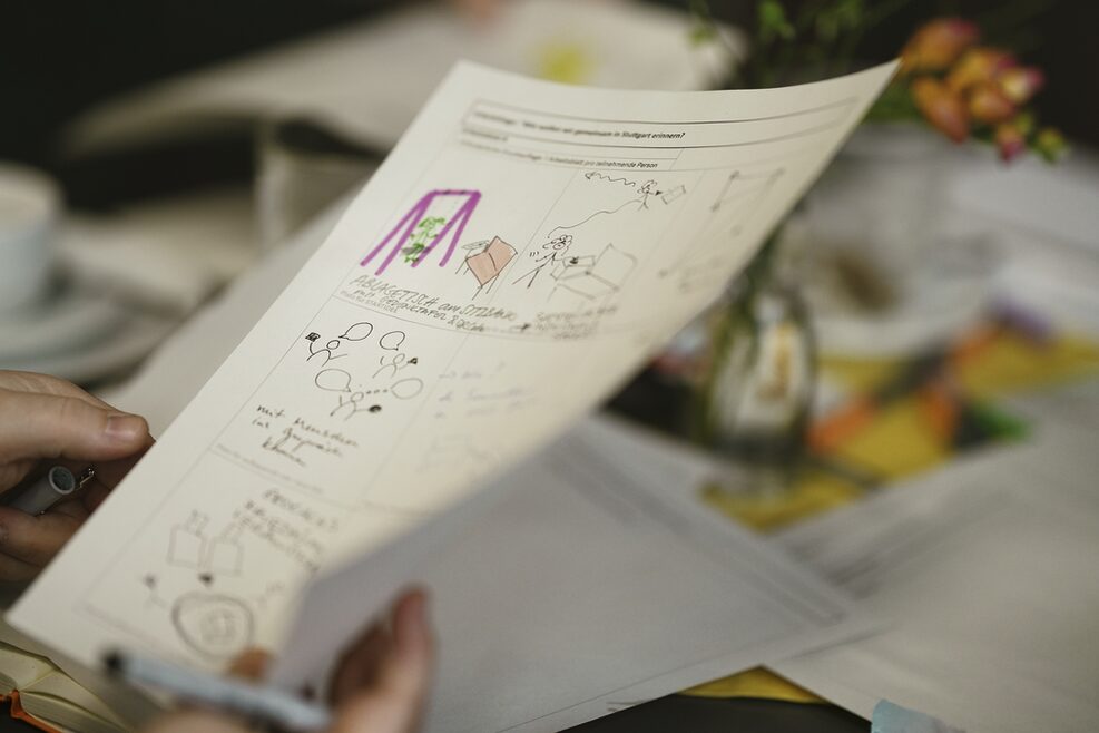Blick auf die Hände einer Person, die ein Blatt mit nicht näher erkennbaren Grafiken in der Hand hält.