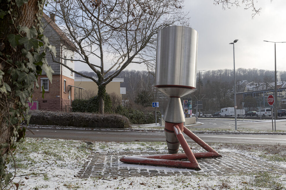 Zylinderförmige Skulptur aus geschliffenem Metall mit rotem Fuß.