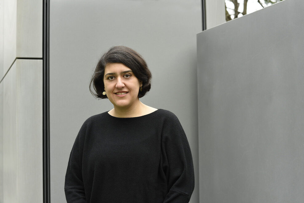 Foto von Elnaz Seyedi in einem schwarzen Pullover vor einer grauen Wand.