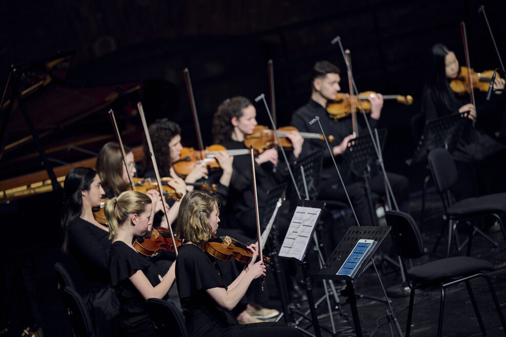 Mehrere Streichmusiker spielen sitzend, schwarz gekleidet auf einer schwarzen Bühne.
