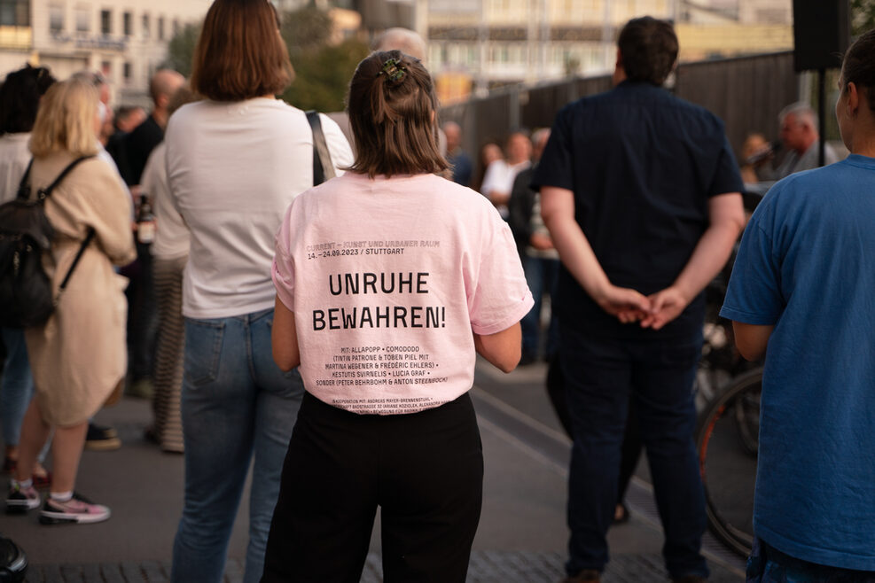 Mehrere Menschen von hinten auf einem T-Shirt steht "Unruhe Bewahren!"