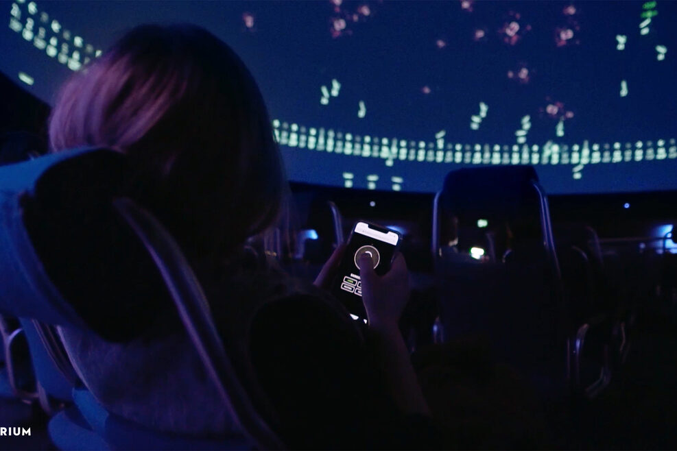 Ein Mädchen navigiert mit dem Handy Himmelsobjekte im Planetarium