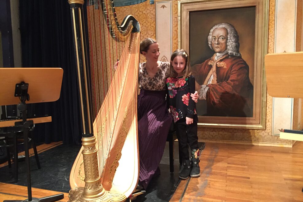 Eine Frau und ein Kind mit großer Harfe vor einem Bildnis von J.S. Bach