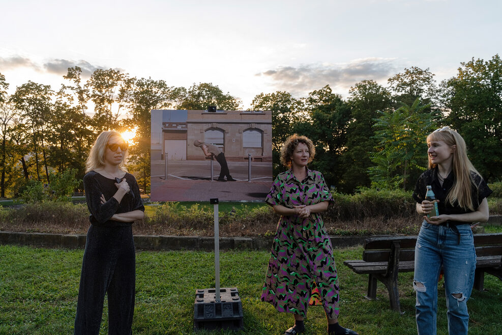 Drei Frauen tauschen sich im Rahmen des Künstlerinnengesprächs zur Ausstellung "Exploring the City" vor einer Fotografie im Park der Villa Berg aus.