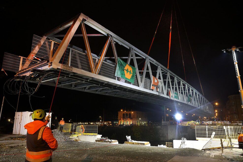 Ein Bauarbeiter hilft bei Dunkelheit auf der Baustelle beim Einheben der neuen Behelfsbrücke über den Neckar.