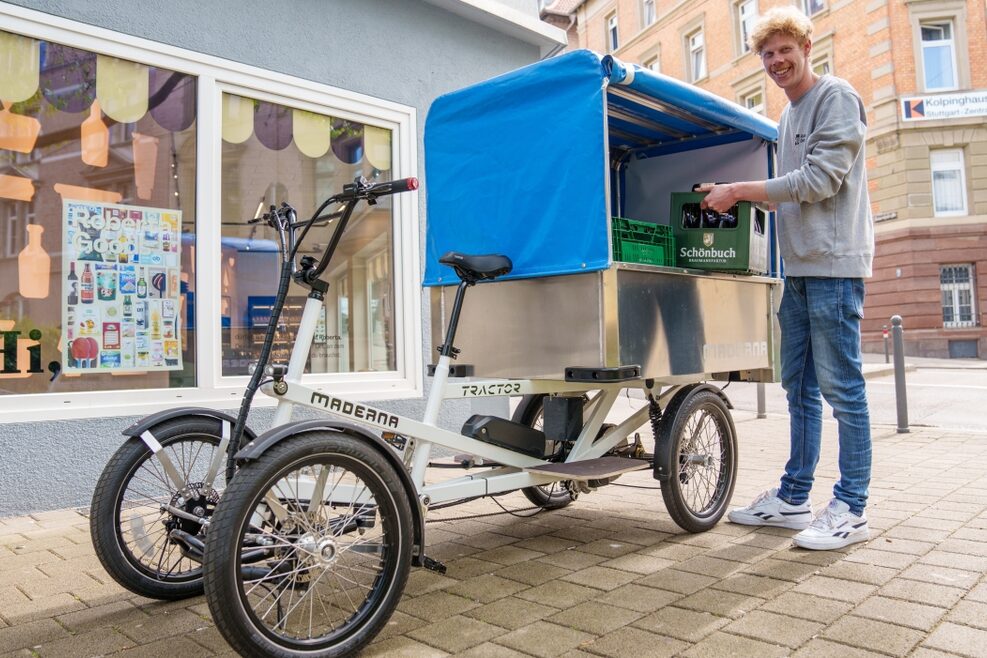 Ein junger, fröhlicher MAnn belädt ein Lastenrad und lächelt in die Kamera.