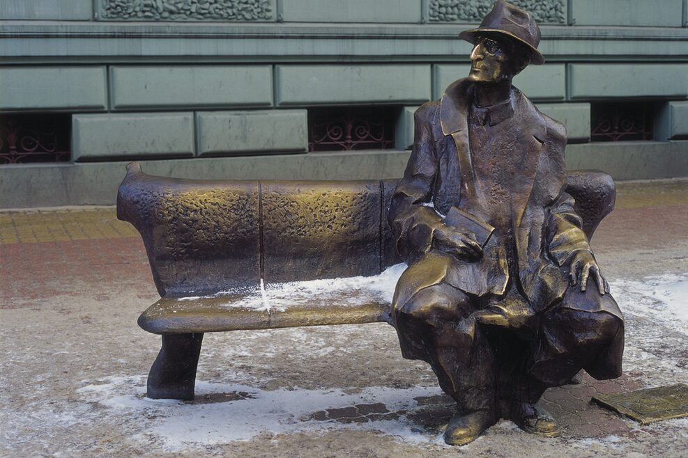 Bronzestatue eines Mannes, der auf einer Bank sitzt.