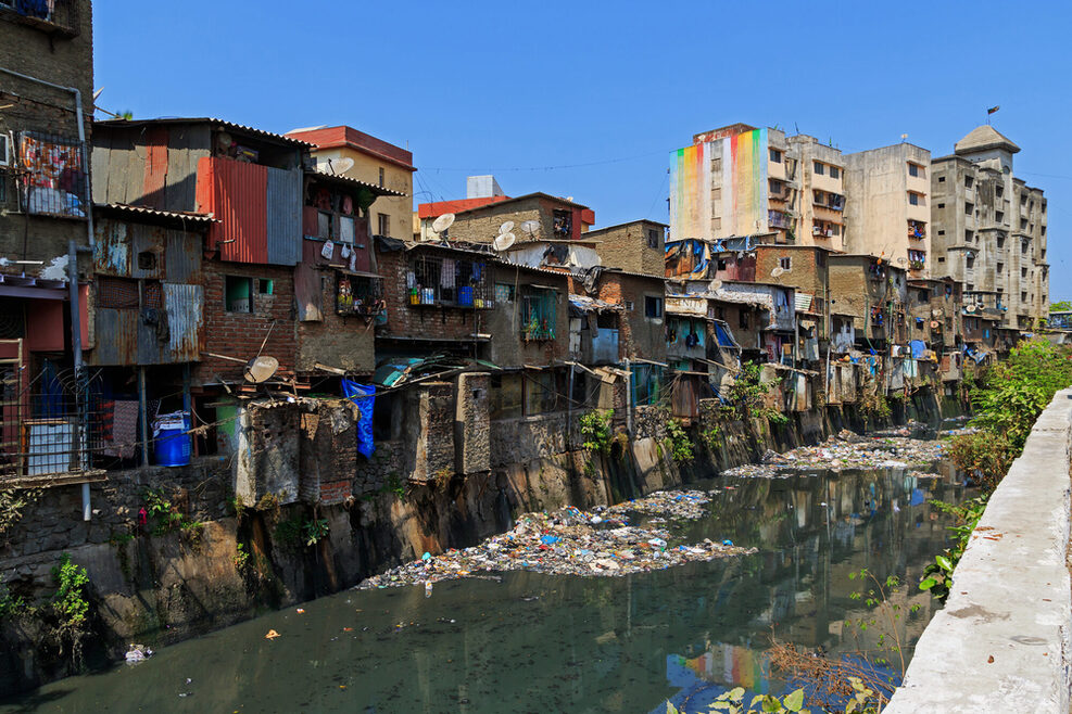 Viele Häuser nebeneinander an einem Kanal in einem Slum in Mumbai
