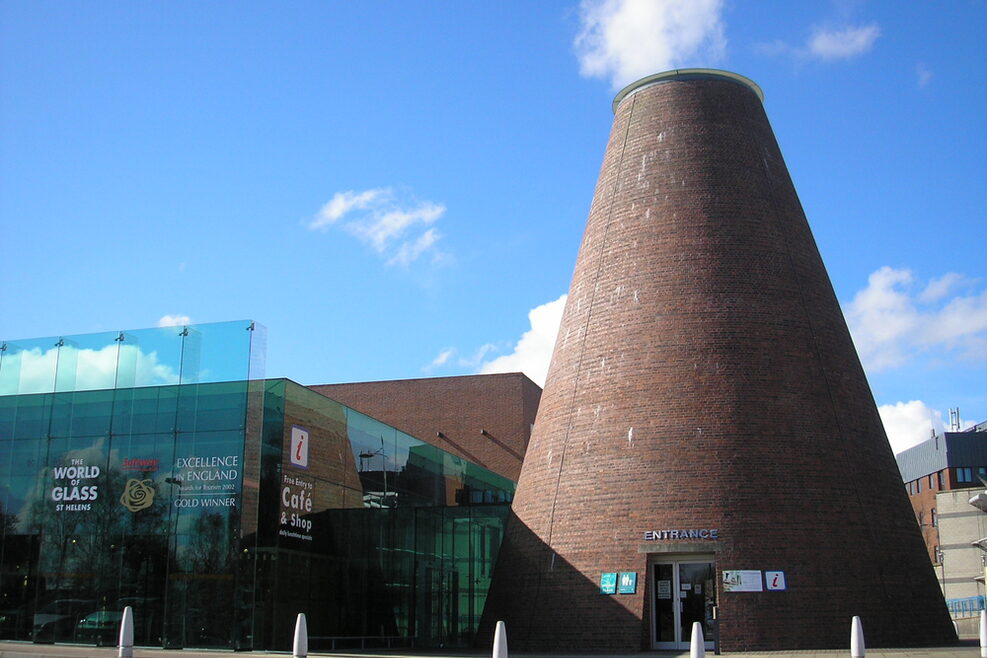 Ein kegelförmiges Gebäude und ein Kubus aus Glas stehen nebeneinander.