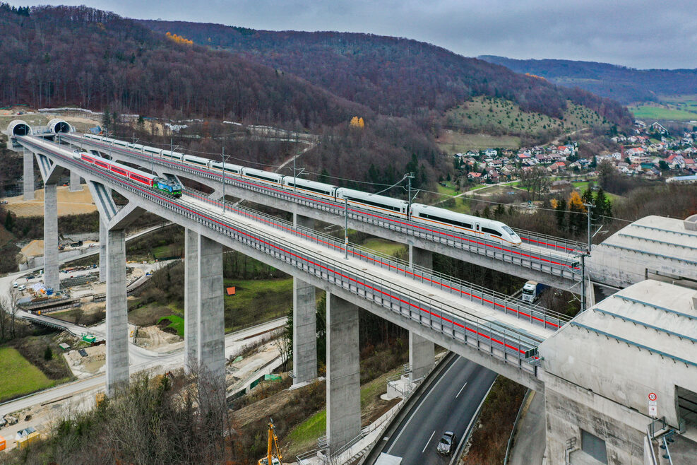 Auf den zwei Gleisen fahren parallel nebeneinander links eine Regionalbahn und rechts ein ICE die Filstalbrücke entlang.