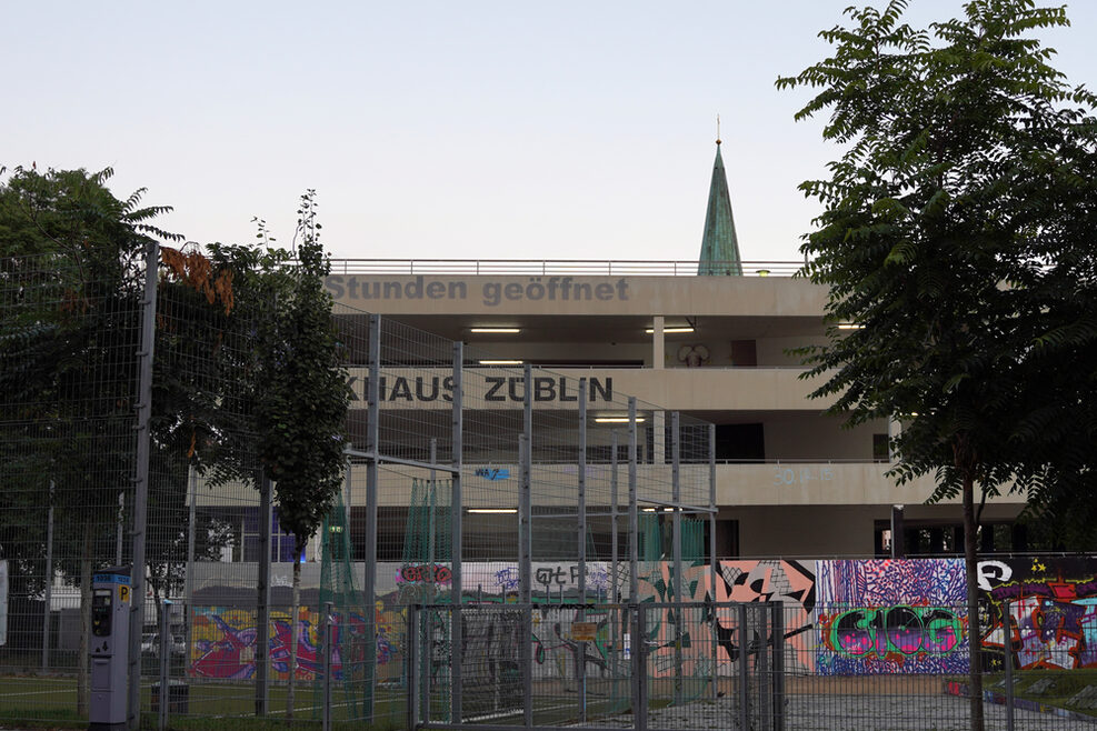 Fassade des Züblin Parkhauses mit bunten Graffiti im Hintergrund, vorne ein Sportplatz