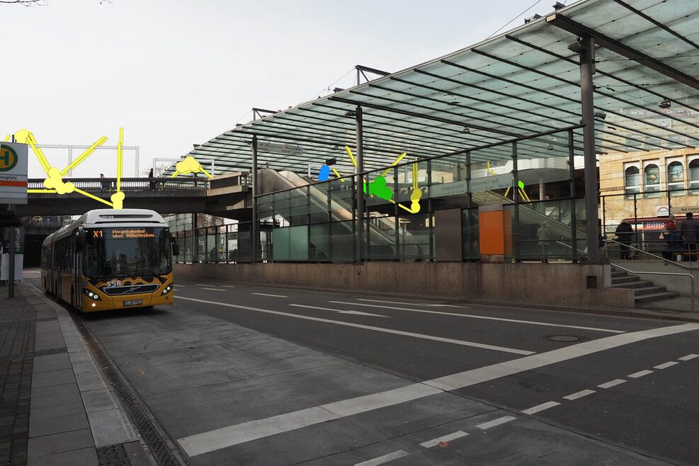 Fotomontage: Die Ansicht des Wilhelmplates von der Straßenebene aus, mit Holzlatten werden bunte Figuren entlang der Station angebracht.