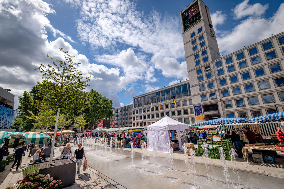 Blick auf den Marktplatz mit dem neuen Wasserspiel. Es ist Markt. Im Hintergrund ist das Stuttgarter Rathaus zu sehen.