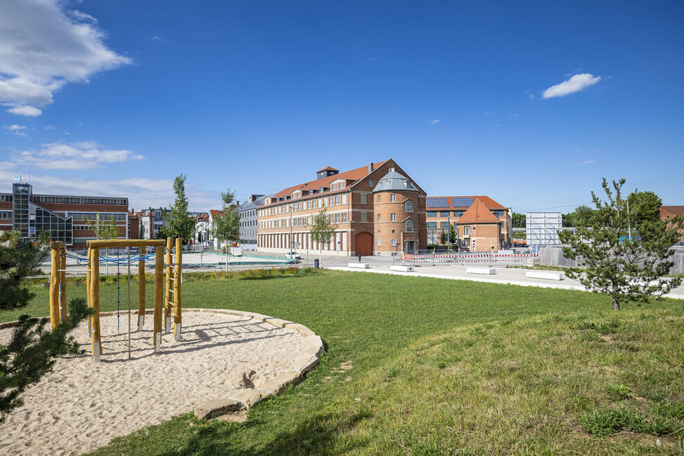 Blick auf einen Spielplatz, Wiese und mehrere Gebäude im Hintergrund.