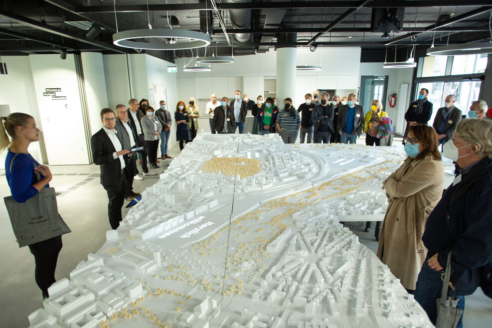 In der Mitte des Bildes steht das Stadtmodell, um das sich rund 40 Menschen versammelt haben. Im Hintergrund sind weitere Teile der Ausstellung zu erkennen.