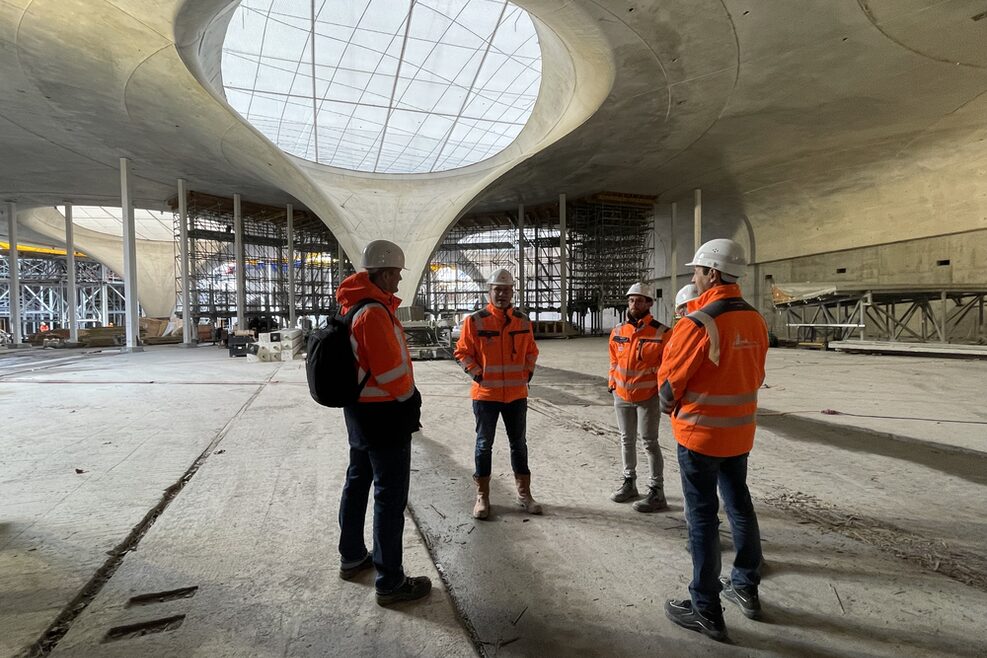 Fünf Personen stehen im Bereich der späteren Bahnhofshalle mit Blick auf die Kelchstützen und das Schalendach.