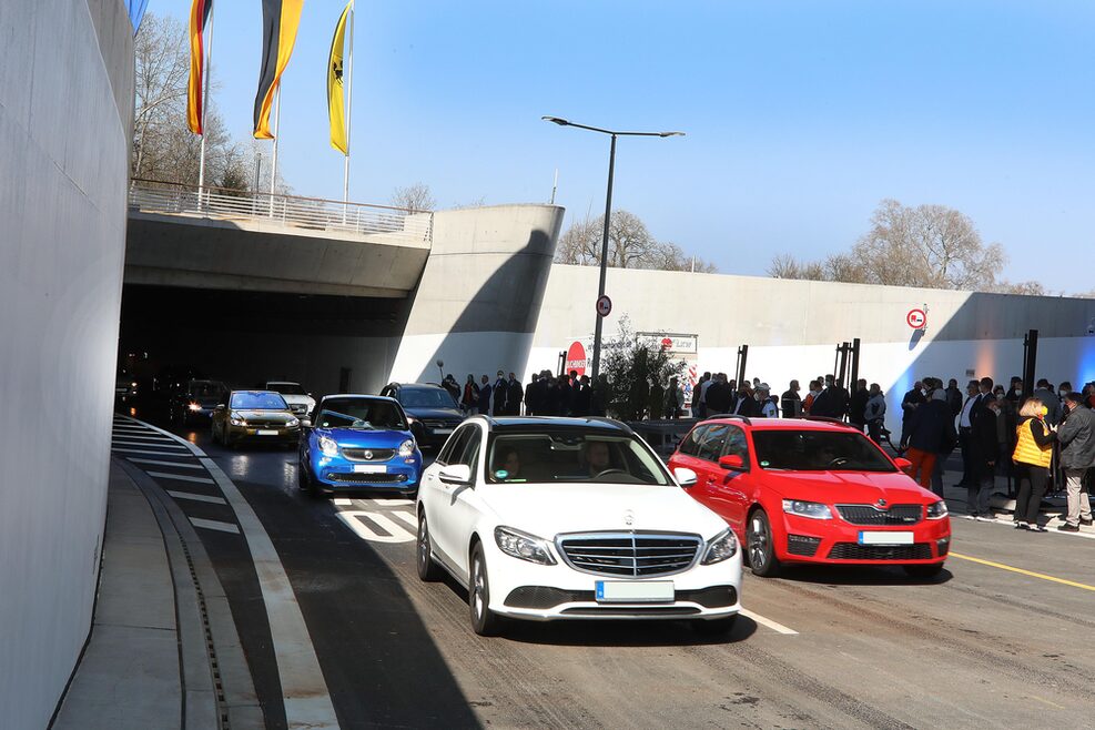Die ersten Fahrzeuge kommen aus dem Tunnelportal nahe der Wilhelma. Rechts stehen in einem sicheren Bereich Bürgerinnen und Bürger, die die Autofahrer begrüßen.