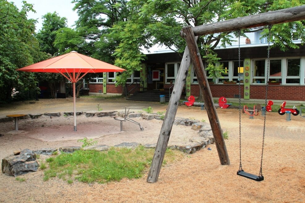 Auf dem Spielplatz gibt es einen großen Sandkasten und viele Schaukeltiere.