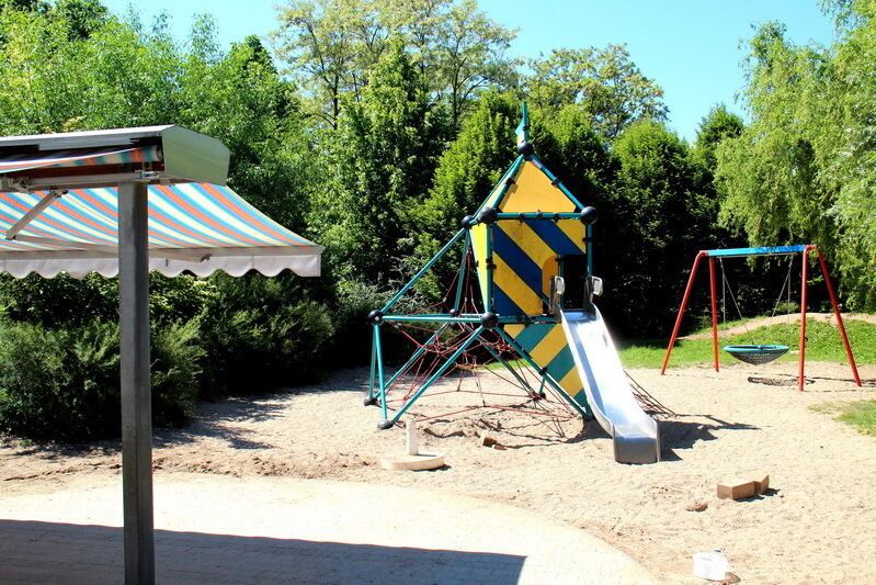 Außenbereich mit Klettergerüst, Schaukel und Rutsche auf Sandboden.