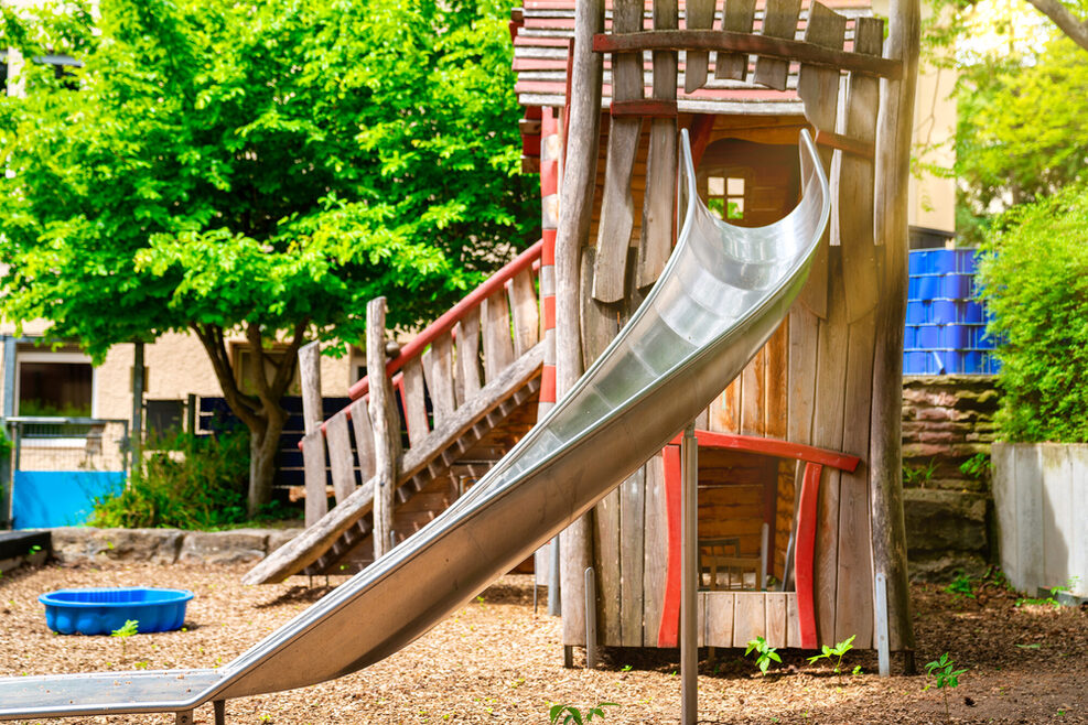 Auf dem Spielplatz steht ein Spielturm zum Klettern mit einer Rutsche.