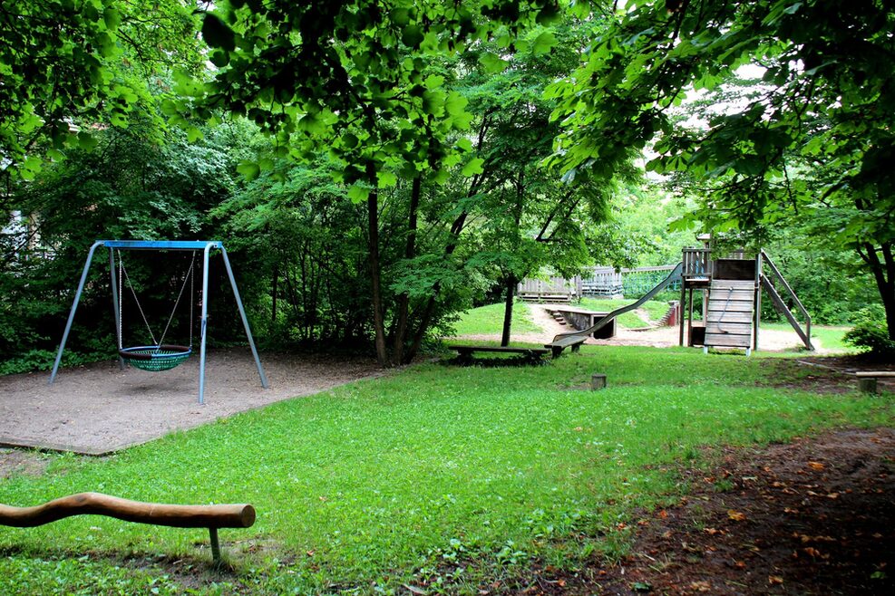 Blick auf den gesamten Spielplatz mit Korbschaukel und Balancierstange.