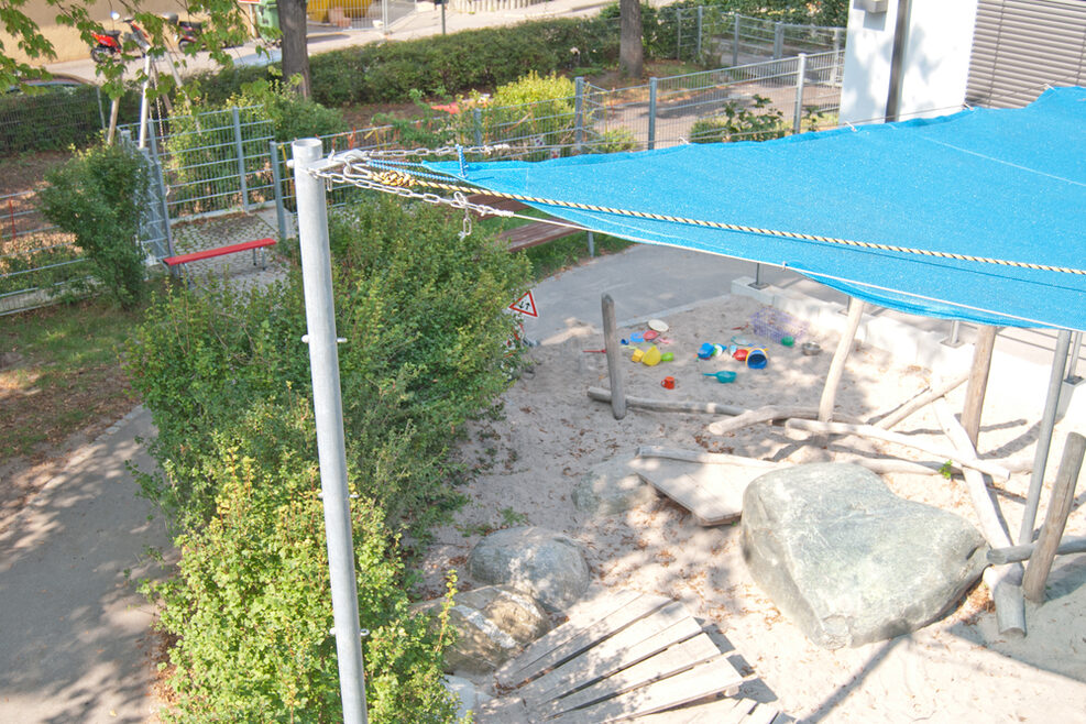 Der überdachte Sandkasten mit Holzstämmen und Steinen zum Balancieren.